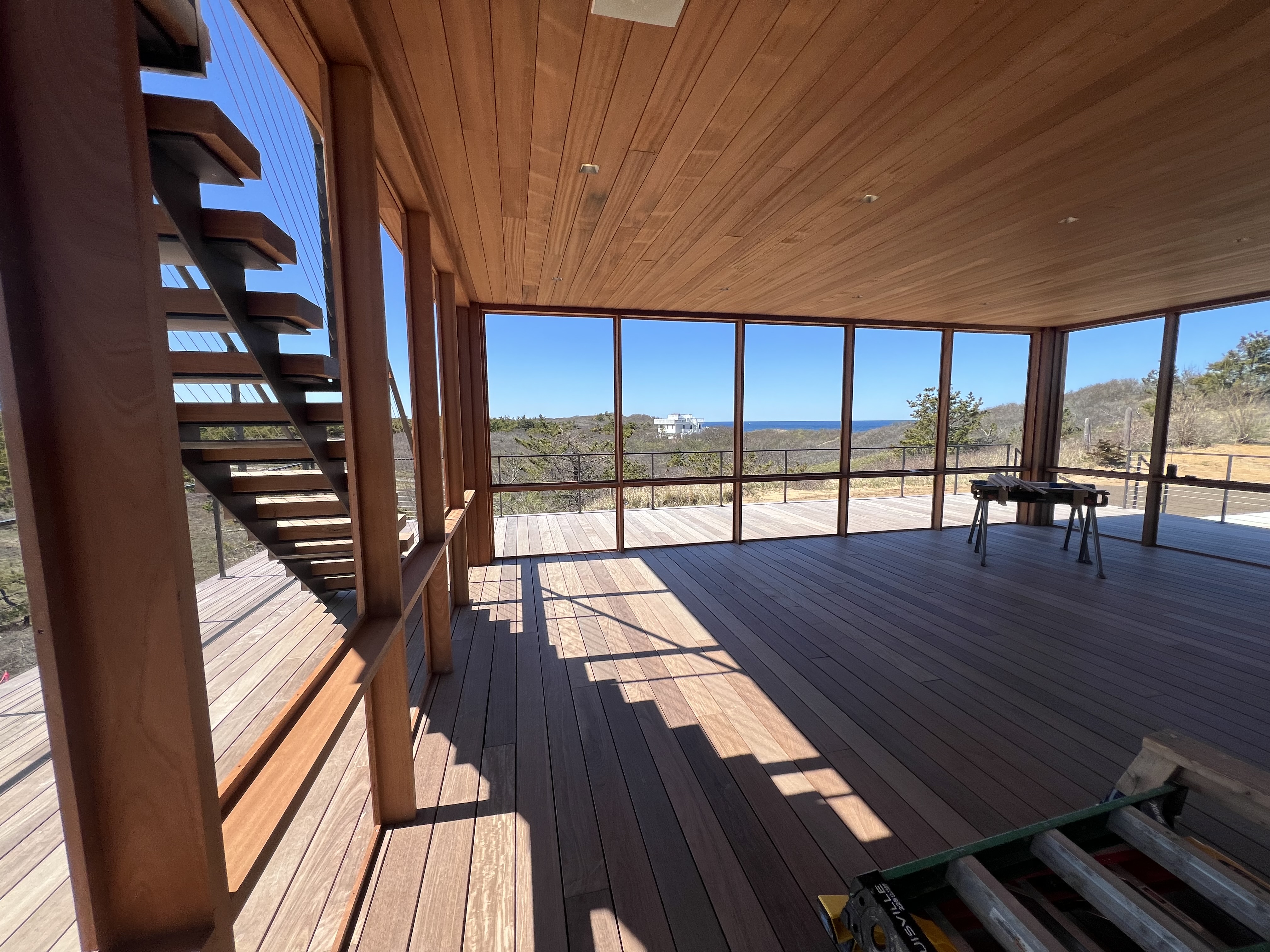 Screened deck with wood ceiling, open stairs, and ocean view.